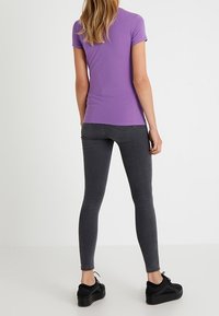 Paarse kortearm T-shirt gecombineerd met donkere grijze skinny jeans en zwarte platform sneakers, met een gladde stoftextuur.