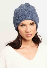 Kötött kék sapka bordás textúrával, amelyen egy kis ezüst gomb részlet található az oldalán. Meleg és kényelmes kialakítás.