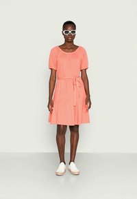 Vestido coral com mangas curtas bufantes, cintura atada e saia em camadas. Textura suave e tecido leve complementam o estilo casual.