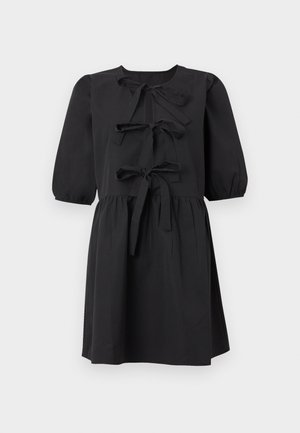 Robe noire à manches courtes avec trois nœuds sur le devant, taille froncée et encolure ronde sur un fond uni.