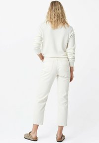 Suéter blanco, jeans cortos blancos y zapatos slip-on beiges. El material parece suave, con costuras visibles y dos bolsillos traseros en los jeans.