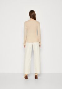 Beige Longsleeve-Oberteil kombiniert mit weißen, weit geschnittenen Hosen, die ein einfaches Design und einen strukturierten Stoff aufweisen. Braune Blockabsatzschuhe sind enthalten.