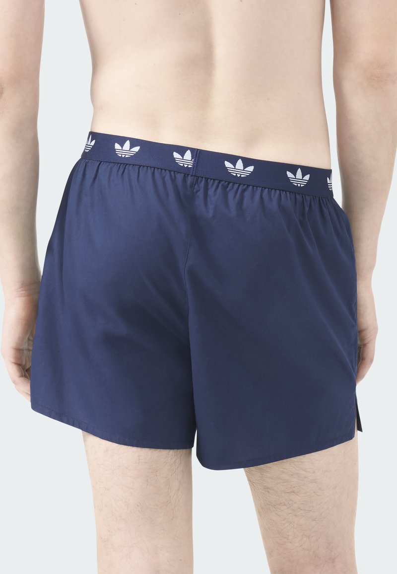 Marineblaue Badeshorts aus leichtem Stoff, mit gemustertem elastischem Bund und seitlichen Schlitzen für mehr Bewegungsfreiheit.