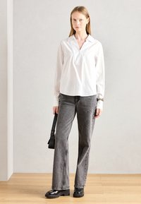 Hvit langermet skjorte med V-hals og stripemønster, sammen med grå vide jeans og svarte platåsko. Svart skulderveske i hånden.