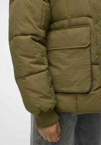 Olijfgroen gewatteerde jas met een gestikte textuur, elastische manchetten en een borstzak. Glad materiaal met een matte afwerking en minimale details.