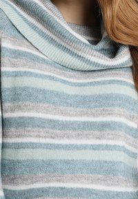 Pull à col cheminée en matière douce, présentant des rayures horizontales en bleu clair, gris et blanc avec une légère brillance et un tricot texturé.