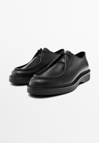 Black leather shoes with a rounded toe, a seam along the upper, and a thick black sole. The design features no visible hardware or patterns.