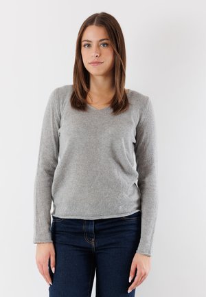 Maglione grigio a maglia con scollo a V, maniche lunghe e vestibilità comoda, abbinato a jeans blu scuro. Texture morbida e aspetto semplice.