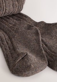 Brązowe, dziergane skarpetki o prążkowanej fakturze i wzorze w warkocze. Miękki, gruby materiał z zaokrąglonym noskiem i wzmocnioną piętą dla trwałości.