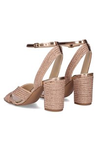 Sandalias de tacón alto en color oro rosa con un diseño de tira texturizada y trenzada, puntera afilada y tacones en bloque gruesos y estriados. Correa ajustable en el tobillo.