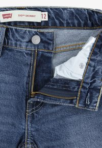 Jeans 510 Skinny de Levi's, en denim azul oscuro, con costuras doradas, cierre de botón y cremallera. La etiqueta de tamaño indica la talla 12.