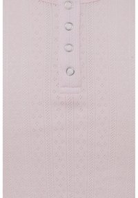 Haut rose pâle côtelé avec un petit rabat à boutons, comportant cinq boutons-pression argentés, et un tissu texturé avec de petits motifs floraux en relief.