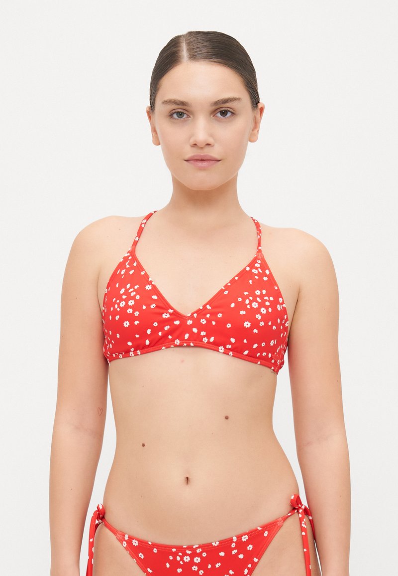 Rød bikini med hvitt blomstertrykk. Toppen har en trekantet fasong og tynne stropper; bunnen har snøring i sidene og et lignende blomsterdesign.