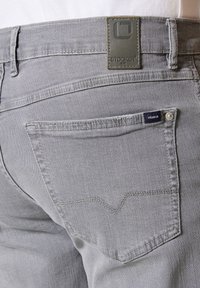 Pantalones de mezclilla gris con un acabado texturizado, con una etiqueta de cuero que dice "STOKER", dos bolsillos traseros con detalles de costura y un corte clásico.