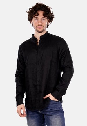 Maglietta nera a maniche lunghe realizzata in tessuto strutturato con colletto alla cinese. Presenta una chiusura frontale con bottoni. Indossata con jeans di denim.
