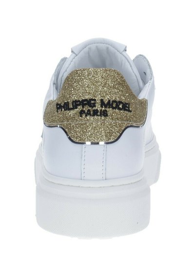 Sneaker bianca con un inserto glitterato oro sul tallone. Presenta un testo logo nero e una finitura in pelle liscia. Suola spessa bianca per un buon ammortizzamento.
