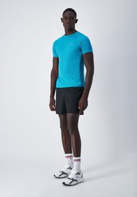 Completo sportivo maschile composto da una maglietta aderente a maniche corte di un vivace turchese e pantaloni corti neri, abbinati a scarpe da ginnastica bianche e calzini a righe.
