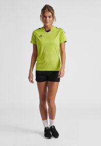 Lys grøn atletisk skjorte med korte ærmer, sort kant ved kraven, parret med sorte shorts. Modellen har sorte sko og hvide sokker på.