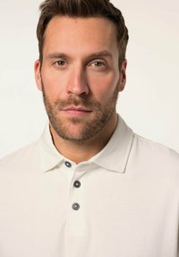 Polo shirt a collo alto in bianco sporco, con apertura a tre bottoni in grigio scuro, realizzato in tessuto morbido con una leggera lucentezza.