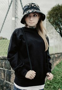 Maglione nero con scollo rotondo e coulisse, abbinato a un cappello a secchiello con motivo floreale. Caratterizzato da una vestibilità comoda e maniche lunghe.