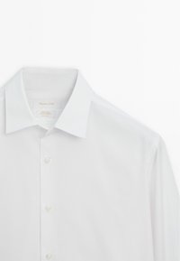 Hvid skjorte med spidst krave og knaplukning foran, lavet af letstrygeligt italiensk stof, vist på en ensartet hvid baggrund.