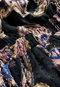 Zwarte stof met ingewikkelde paisley-patronen in roze, blauw en goud. Textuurrijke details en een opvallend gerimpeld ontwerp.