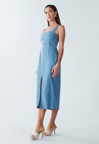 Zila midi kleita ar kvadrātveida kakla izgriezumu, priekšējo pogu aizdari un sānu šķēlumu. Raksturīga plānas lencītes un gluda, fakturēta auduma.