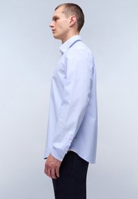 Lichtblauwe blouse met lange mouwen, kraag, knoopmanchetten en zijsplitten. Heeft een subtiele textuur en een contrasterende accentkleur op de manchetten.