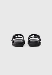 Black platform sandals with adjustable straps and buckles, viewed from the back on a plain light gray background.