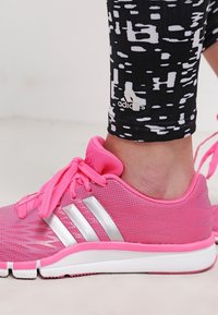 Vaaleanpunaiset urheilukengät, joissa on verkkopäällinen, hopeiset raidat ja vaaleanpunaiset nauhat. Yhdistetty mustiin leggingseihin, joissa on valkoinen abstrakti kuvio.