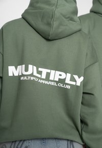 Sweat à capuche vert avec la capuche relevée, arborant un texte blanc audacieux "MULTIPLY" et un texte plus petit "MULTIPLY APPAREL CLUB" au dos.