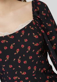 Abito nero a fiori con piccoli motivi di rose rosse, scollatura quadrata e delicata finitura in pizzo bianco. Maniche a palloncino con dettagli arricciati.