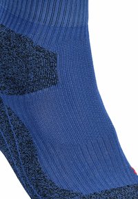 Calcetín deportivo azul con parte superior acanalada, panel negro texturizado y talón reforzado. Acabado suave con un acento rojo.
