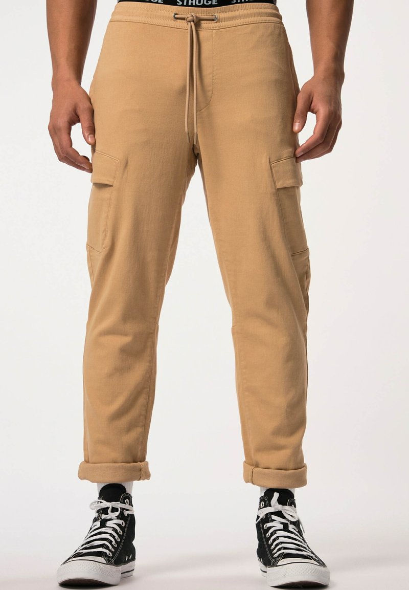 Tarnfarbene Cargo-Hosen mit einem Kordelzugbund, zwei Seitentaschen und umgeschlagenen Säumen, kombiniert mit schwarzen High-Top-Sneakers.