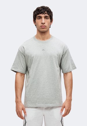 Ung mand, der står frontalt, iført en lysegrå Nike T-shirt og hvide perforerede sportsshorts med sorte striber.
