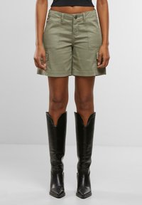Olivenfargede cargo-shorts med knappelukking, som har to frontlommer og sidelommer. Kombinert med høye svarte støvler.