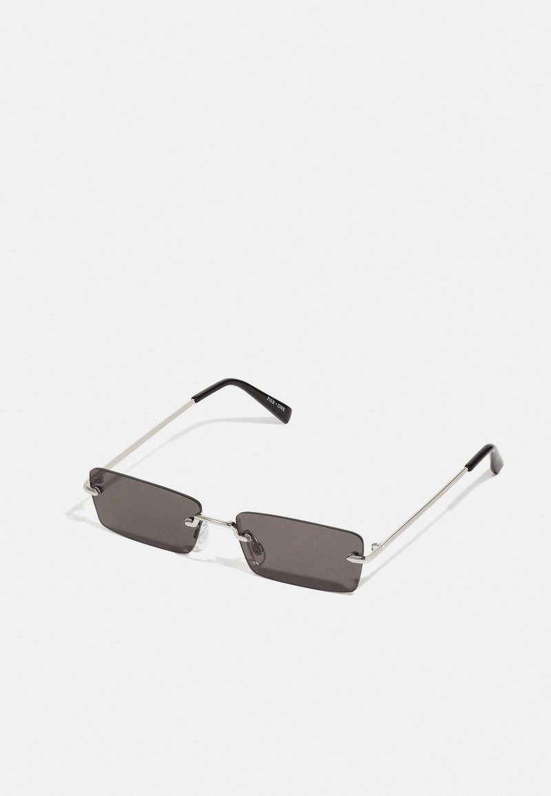 Óculos de sol com lentes retangulares, cinzentas escuras, armações em metal prateado e pontas em plástico preto nas hastes. Design leve com almofadas para o nariz.