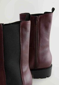Botine burgundy cu panouri laterale elastice negre, finisaj din piele netedă și talpă din cauciuc rezistentă. Închidere cu fermoar pe partea exterioară.
