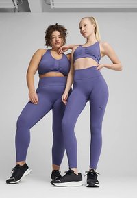 Set paarse sportkleding bestaande uit een aansluitende crop top met textuur en een hoge taille legging, gecombineerd met zwarte sneakers.