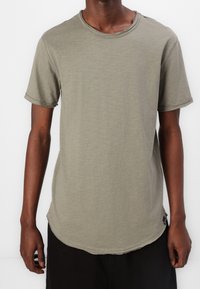 Olijfgroen T-shirt met korte mouwen van zachte stof, voorzien van een ronde halslijn, onafgewerkte randen en een gebogen zoom aan de onderkant. Subtiele logo-label aan de zijkant.