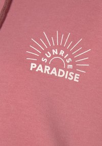 Felpa rosa con texture morbida, caratterizzata da una stampa bianca con la scritta "SUNRISE PARADISE" e raggi che si estendono intorno al testo.
