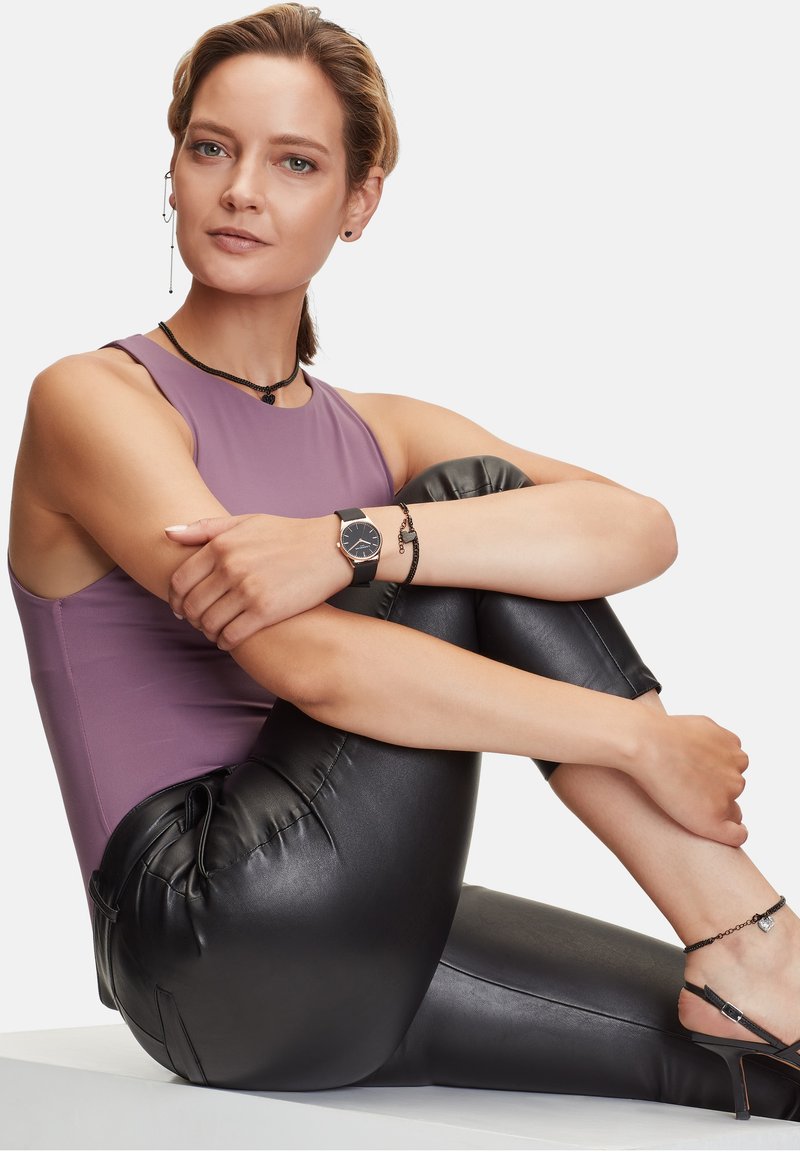 Paarse mouwloze top, zwarte neplederen legging, zwart horloge, bijpassende sieraden, gladde textuur en minimalistisch ontwerp.