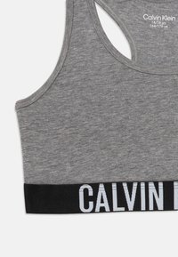 Pilkas sportinis liemenėlė, pagaminta iš minkštos medžiagos; turi juodą juostą su baltu tekstu "CALVIN KLEIN"; dizainas su lenktu nugara ir lygiomis kraštinėmis.