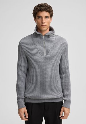 Light grey knit sweater with a high collar and half zip, featuring a textured ribbed pattern and fitted cuffs.