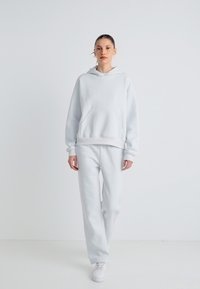 Sweatshirt cinzento claro com capuz e calças de treino a condizer, feitas de tecido macio. Apresenta um bolso frontal e punhos canelados. Usado com ténis brancos.