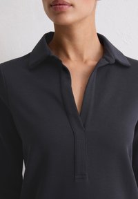 Granatowa koszulka polo z długim rękawem i kołnierzykiem, z rozcięciem na guziki. Tkanina wydaje się gładka i miękka w dotyku.