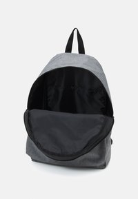 Šedý látkový batoh s velkým černým vnitřkem, zipovým uzávěrem a horní rukojetí. Disponuje jednoduchým designem a lehkým materiálem.