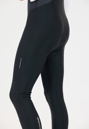 Lähikuva henkilöstä, joka pukeutunut mustiin pyöräilyhousuihin, joissa on pehmustettu istuinosa ja heijastava "Endurance"-logo reisissä.