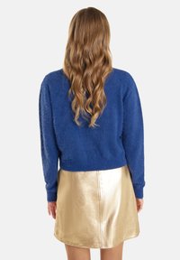 Blauwe pluizige trui met lange mouwen, gedragen met een glanzende gouden A-lijn rok. De trui heeft een ontspannen pasvorm en een gestructureerde afwerking.