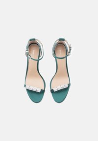 Tyrkysové saténové sandály na podpatku s úzkým páskem kolem kotníku, zdobené rhinestonovým detailem přes nárt, s hladkou texturou.